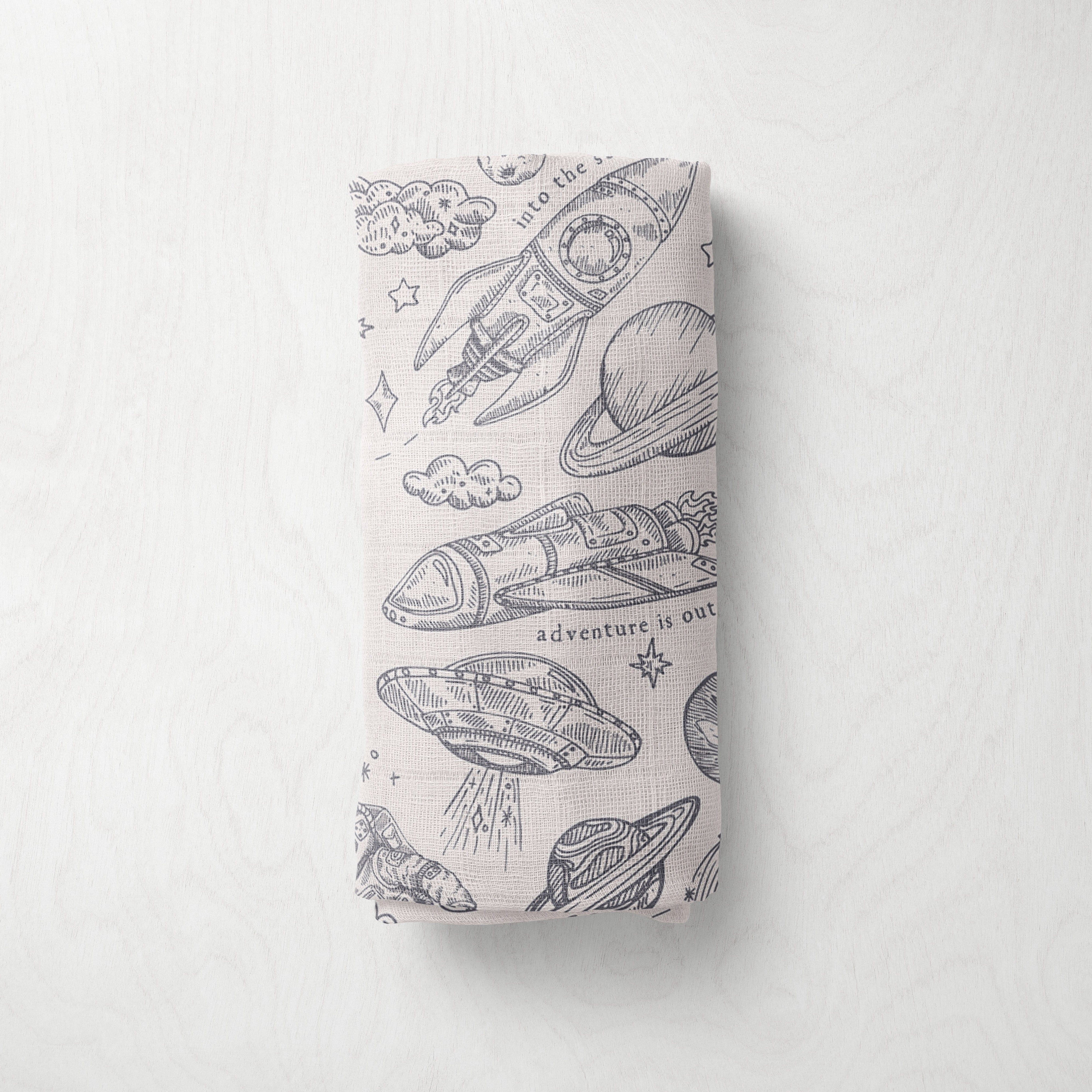 folded muslin swaddle with space-themed pattern on a white background