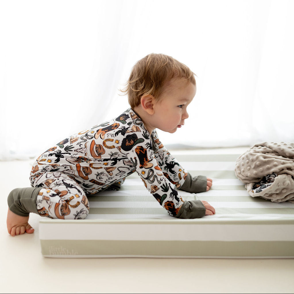 Baby in pajamas crawling on a green and white striped changing mat with a blanket nearby