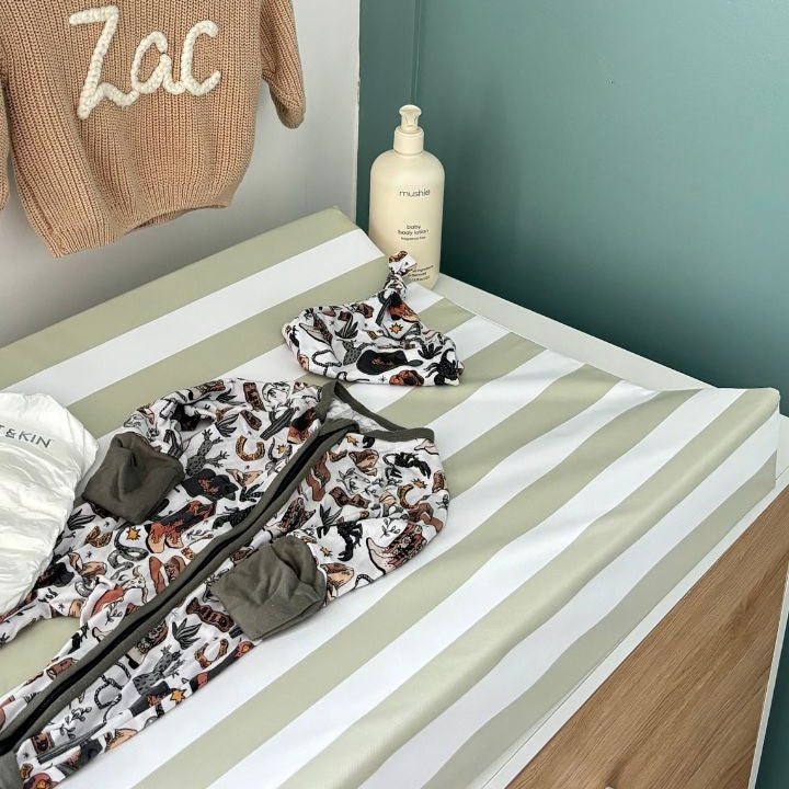 Children's clothing and accessories on a striped changing mat with a plain wall background